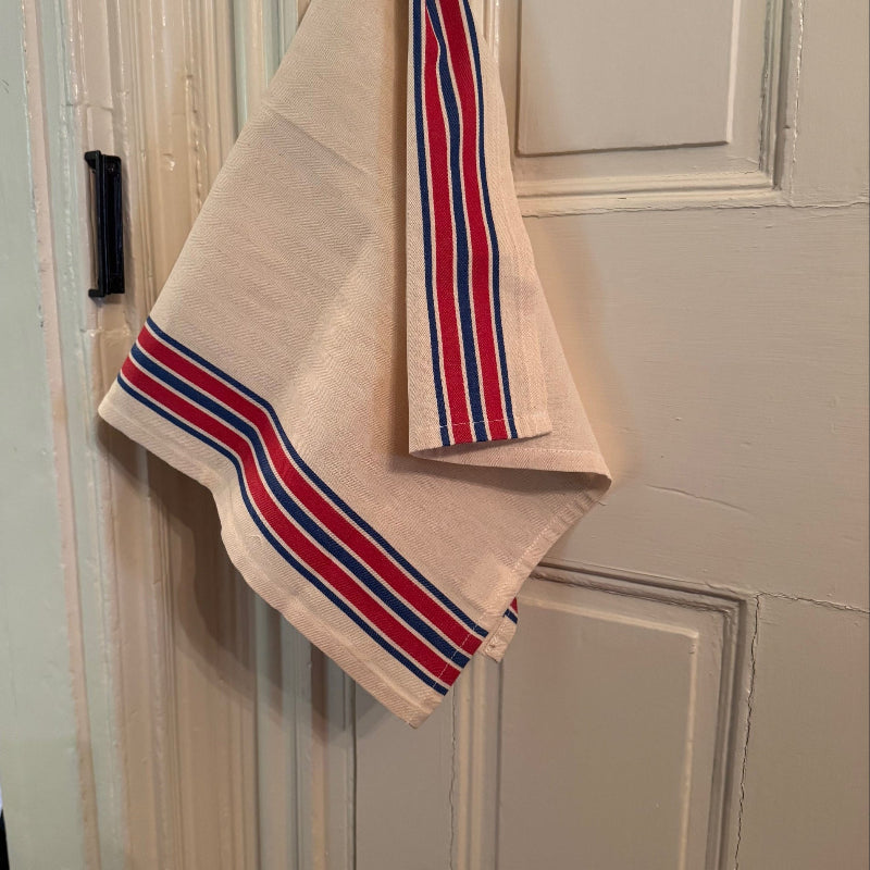 Red and blue striped tea towel hanging on front of white door.