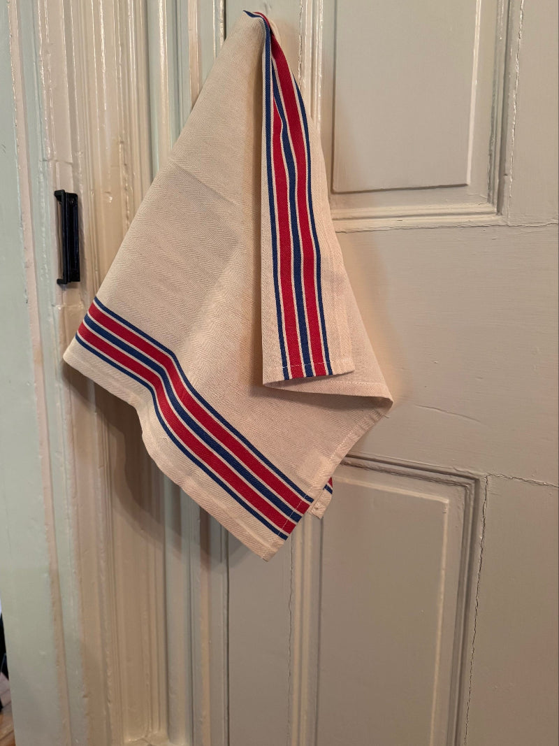 Red and blue striped tea towel hanging on front of white door.