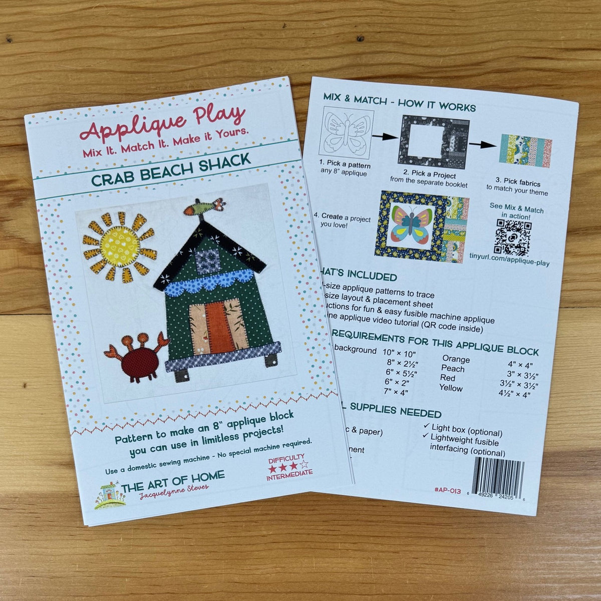A sewing pattern booklet titled 'Applique Play' featuring a crab and beach shack by The Art of Home, showing the front cover and back instructions on a light wood background.