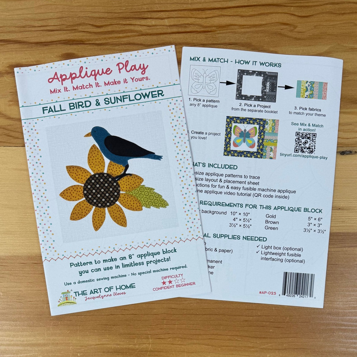 Front and back cover for 'Fall Bird & Sunflower' Applique Play displayed on a light brown wooden tabletop. The front card features a colorful illustration of a blue bird and yellow sunflower, while the back card displays step-by-step instructions, a QR code, and a list of included materials.