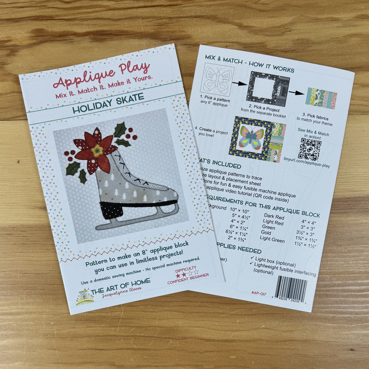 Front and back covers of pattern titled 'Applique Play' and 'Holiday Skate' laid on a wooden surface. The front card shows a colorful applique design of a skater with a red hat and green holly, and the back card explains how to mix, match, and trace patterns with included pieces and measurements.