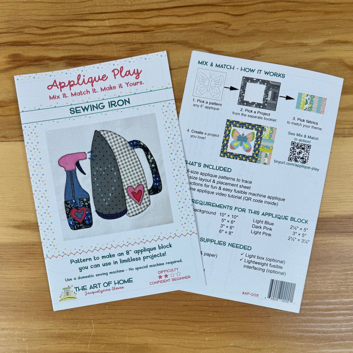 Front and back covers for sewing iron applique pattern sheets laid on a wooden surface. The front sheet shows the product title 'Applique Play', a sewing iron illustration, and instructions; the back sheet shows included materials and requirements.