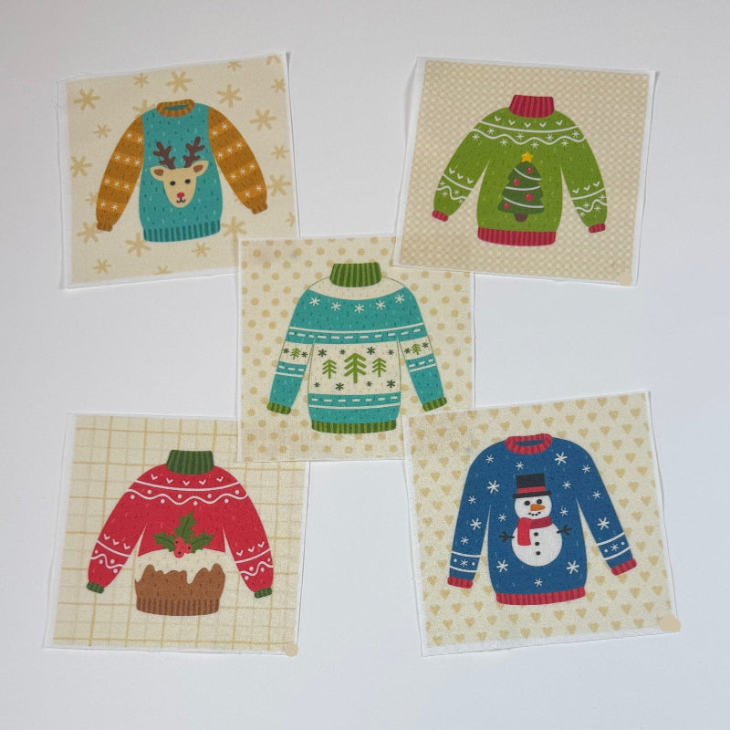 Five small square fabric patches featuring different colorful Christmas sweater designs, arranged on a white tabletop.