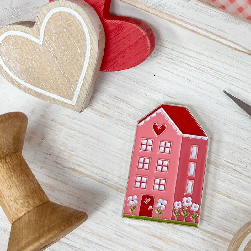Heart-shaped wooden toys and a small house on a wooden surface with a red heart and scissors in the background.