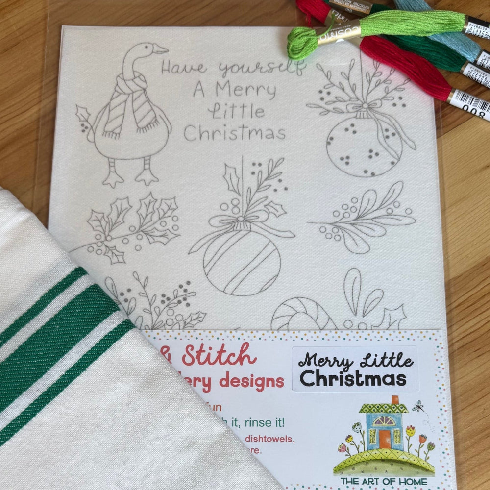 Have Yourself A Merry Little Christmas Stick & Stitch design featuring a Christmas goose, balls, and holly. Includes a green stripe tea towel and embroidery floss on a wood table.