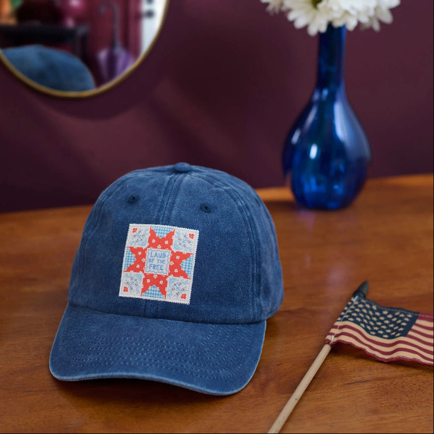 Denim baseball hat sitting on wood top with American Flag and flower vase