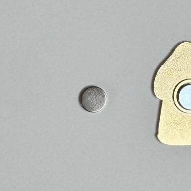 Round replacement magnet for needle minders next to the back of a gold needle minder.