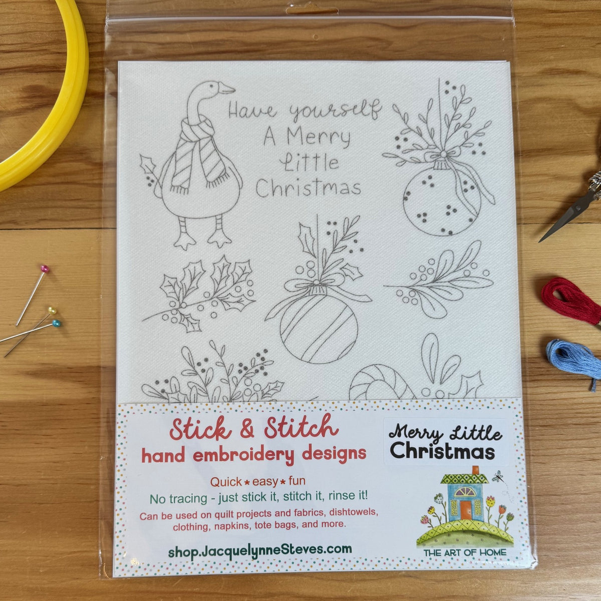 Christmas embroidery designs featuring a goose, balls, mistletoe and holly. Stick & Stitch embroidery sheet on wood table surrounded by sewing notions