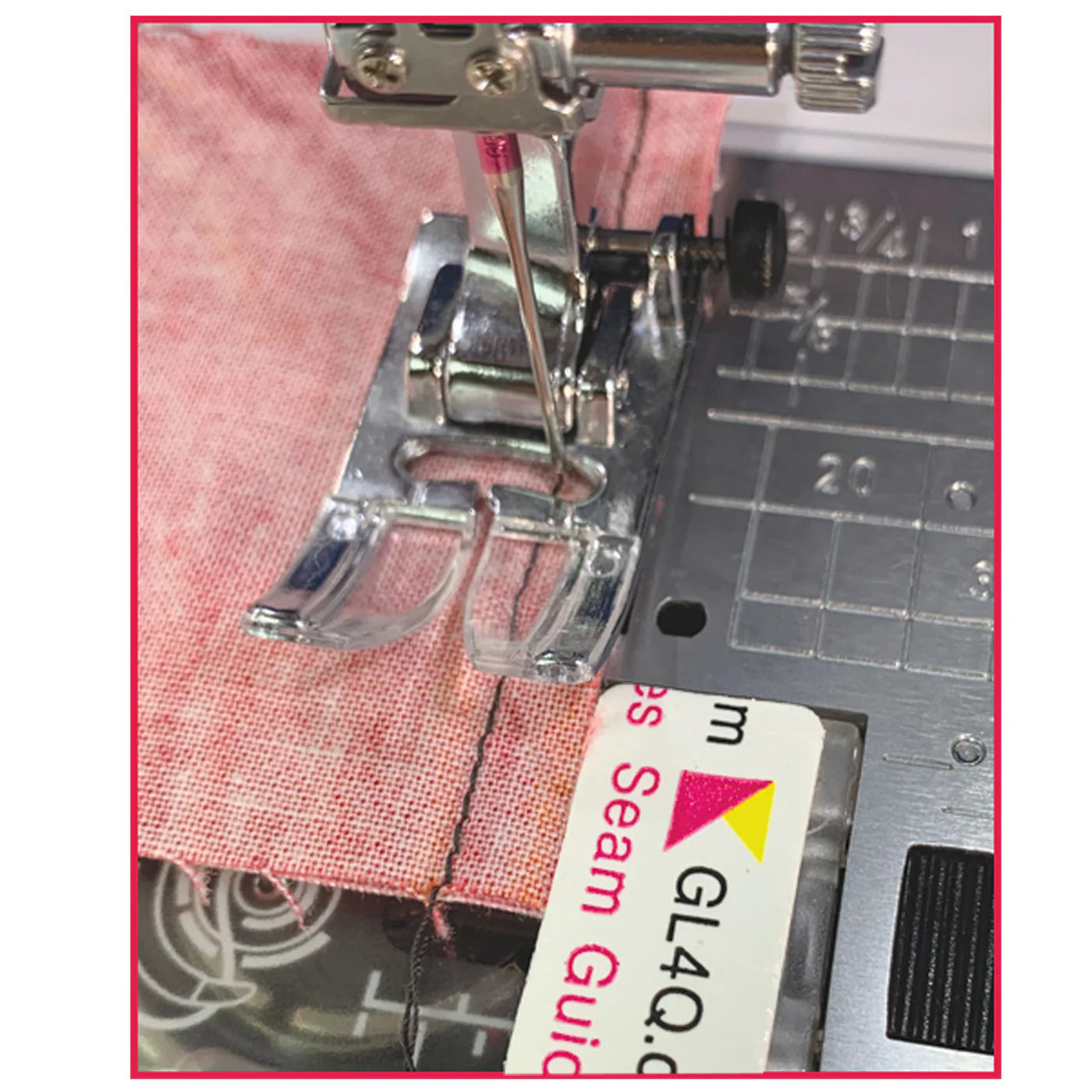 Sewing machine needle and presser foot on pink fabric with a seam guide in the foreground.