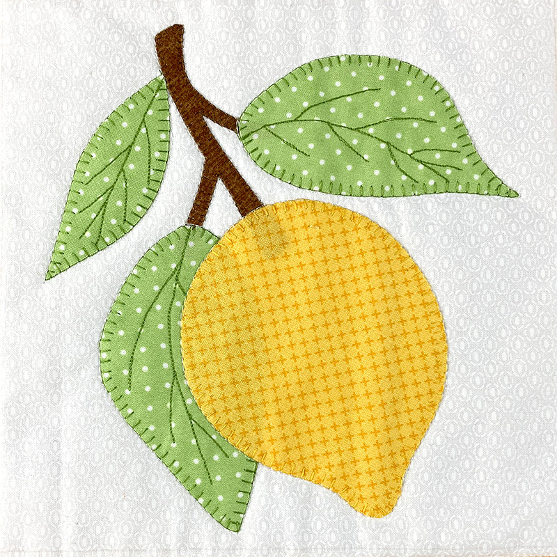 A stylized applique design of a yellow lemon with two green leaves and a brown stem on a white patterned fabric background.