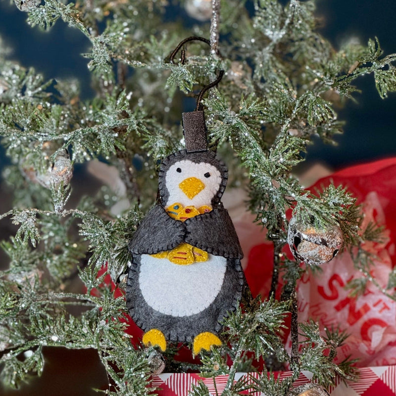 Penguin ornament hanging on a Christmas tree with a wrapped gift underneath.