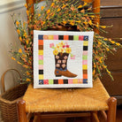 Quilted pillow featuring a cowgirl boot filled with flowers on a wooden chair with a fall flower wreath.