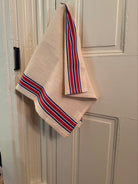Red and blue striped tea towel hanging on front of white door.
