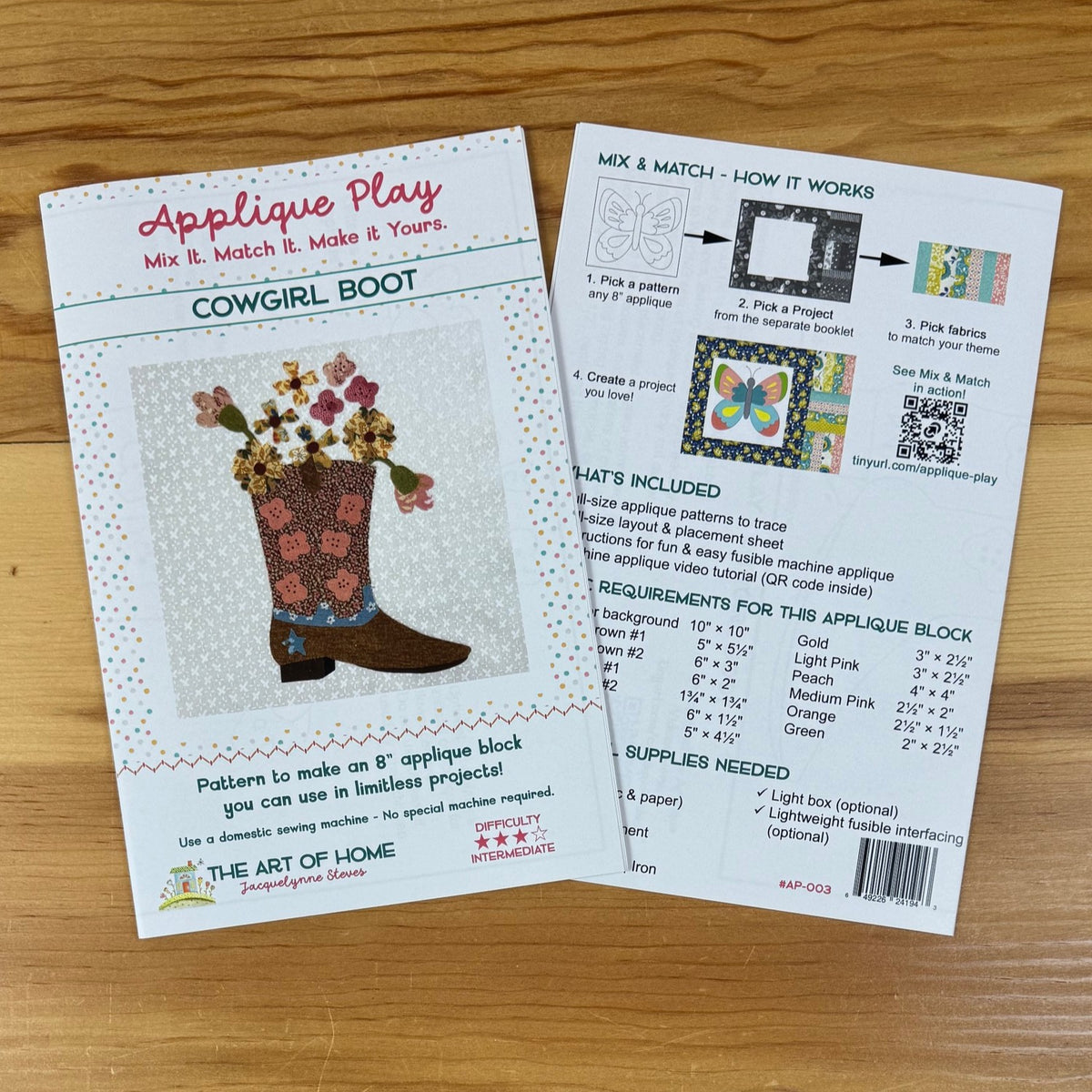 Two printed craft pattern cards for an applique block pattern titled 'Cowgirl Boot' by The Art of Home, placed on a wooden surface. One card shows the front design with a boot and floral applique illustration, and the other shows the back with instructions, included materials, and requirements.