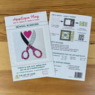 A sewing scissors applique pattern booklet from The Art of Home, displayed on a light brown wooden surface. The front cover shows pink and silver scissors with a pink heart, and the back page includes assembly instructions, a QR code, and a requirements table.