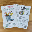 A printed craft pattern sheet titled 'Applique Play: Spring Flower Boots' shown on a wooden surface, alongside the back of the same sheet explaining how to mix, match, and apply the pattern.