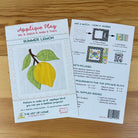 Front and back cover for 'Applique Play' pattern mixing instructions and a sample card for a 'Summer Lemon' applique design, displayed on a light wood surface.