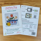 Front and back covers for an applique block pattern titled 'Tulips & Lemon' by The Art of Home, shown on a light wood surface. The front card shows a colorful floral design and instructions, while the back card includes a 'Mix & Match - How It Works' diagram and included supplies list.