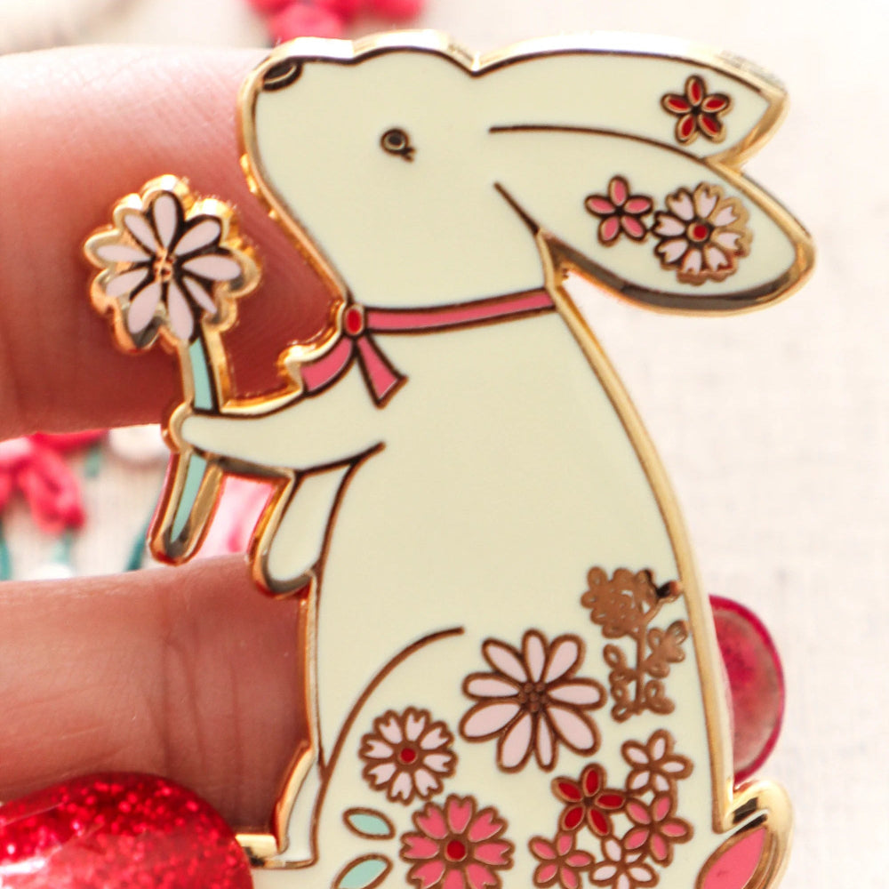 Decorative bunny pin with floral designs held by a hand against a blurred background