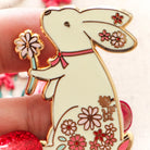 Decorative bunny pin with floral designs held by a hand against a blurred background