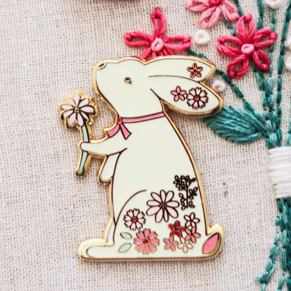 Decorative bunny pin with floral details on a textured fabric background