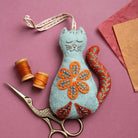 Blue cat-shaped felt ornament with orange folk embroidered designs on a pink background
