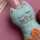 Blue cat-shaped felt ornament with orange folk embroidered designs on a pink background