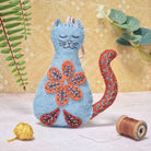 Blue cat-shaped felt ornament with orange folk embroidered designs on a light background