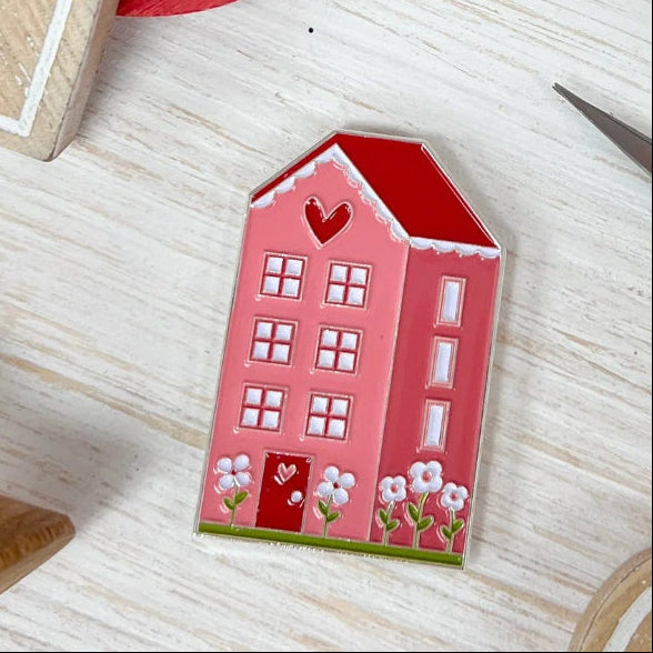 Heart-shaped wooden toys and a small house on a wooden surface with a red heart and scissors in the background.