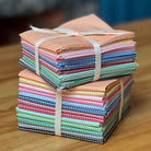 Stack of colorful folded micro gingham cotton tied with a white ribbon on a wooden surface.