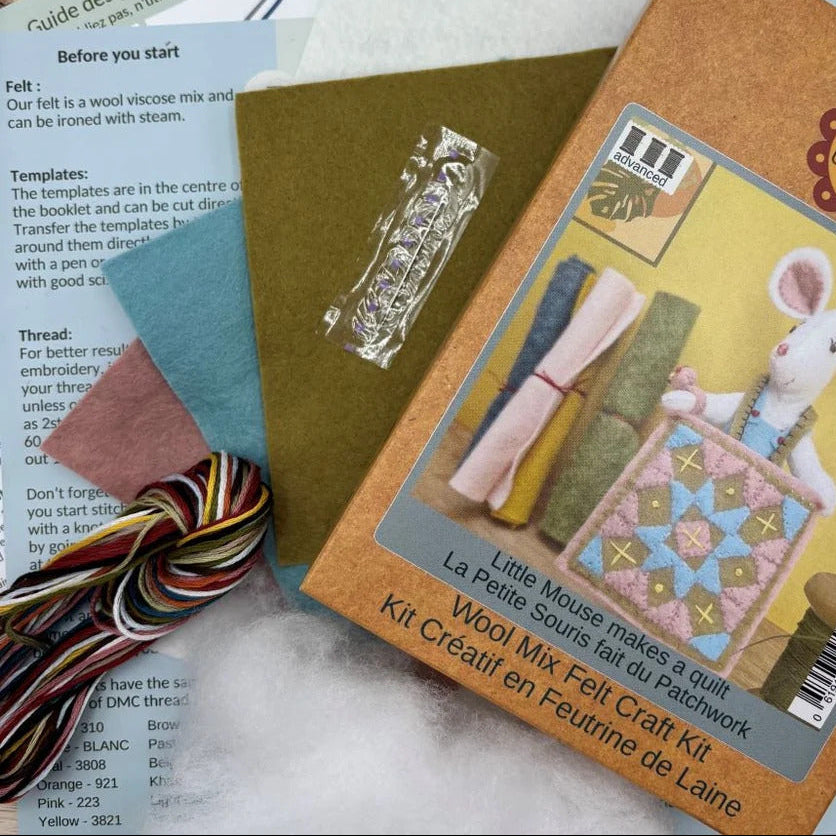 A Little Mice Wool Mix Felt Craft Kit package lying on top of instruction sheets and thread spools. The package is tan with a photo of a white rabbit holding a quilt, and the kit includes multicolored thread, pattern templates, and fabric pieces.