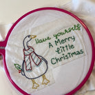 Sample of Merry Little Christmas Stick & Stitch.  Christmas Goose says Have yourself a Merry Little Christmas in a plastic pink embroidery hoop.