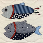 Two stylized fish appliqués on a quilted cream fabric background. The top fish is light blue and navy with red and white striped accents, and the bottom fish is gray and navy with white polka dots and a red stripe.
