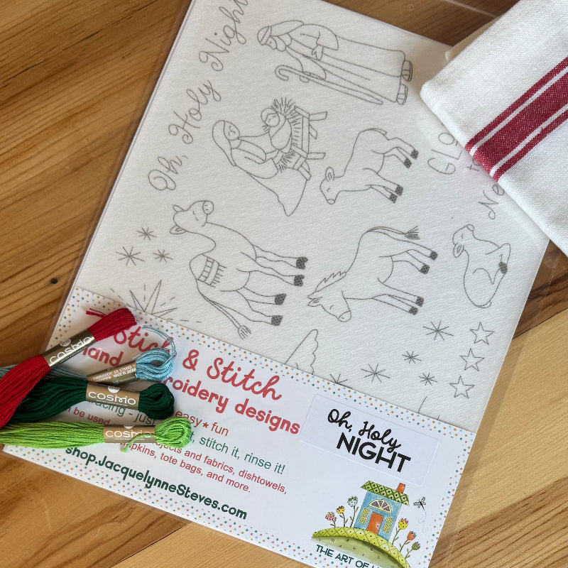 Oh Holy Night Stick & Stitch featuring nativity characters and animals and verbiage.  Also shows red stripe tea towel and embroidery floss on a wood table.