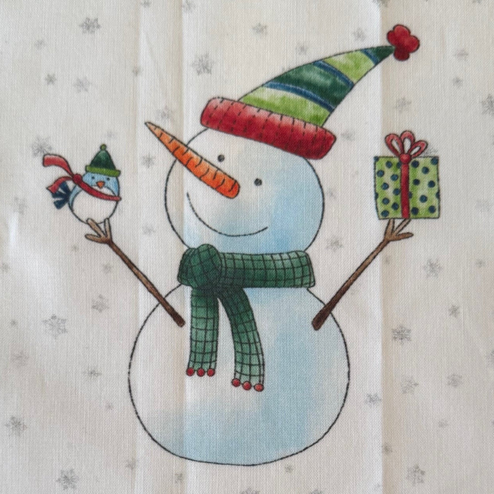 Printed fabric of a snowman with a carrot nose and green hat on a white background.