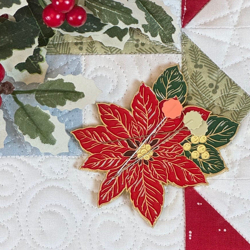 Poinsettia needle minder with pins on Christmas quilt