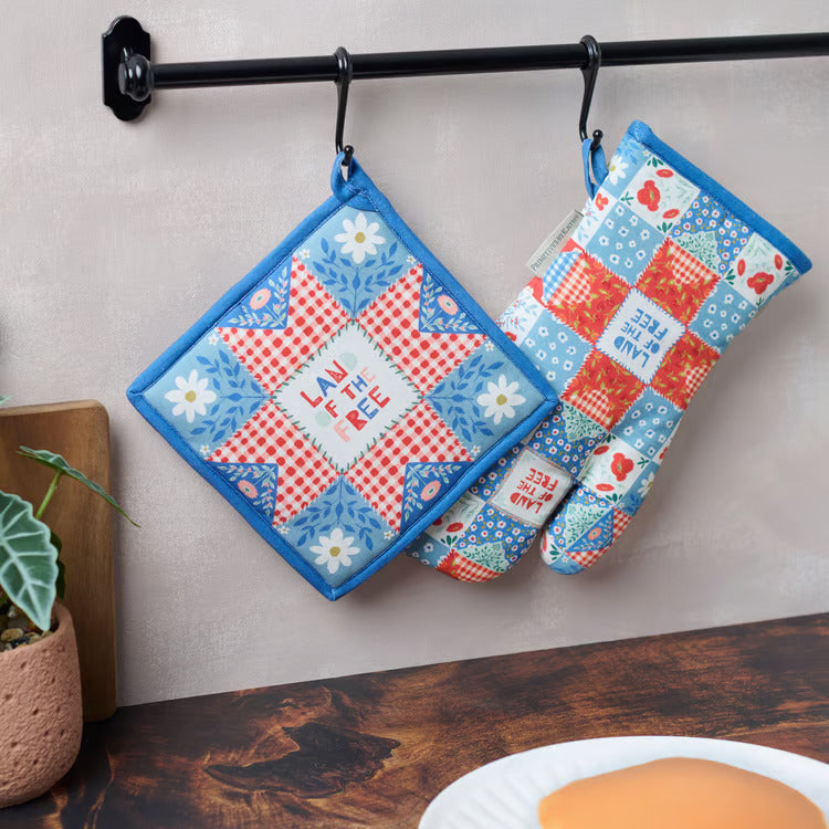 Red white and blue quilt block desing hot pad and oven mitt handing on black towel bar over wood top.