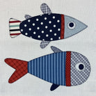 Two handmade patchwork fish appliqués on a light gray fabric background. The top fish has a navy blue body with white polka dots, a light blue head, and a striped tail.