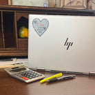 Silver laptop on antique desk with I Love Cross Stitch Sticker and calculator and pens in foreground.