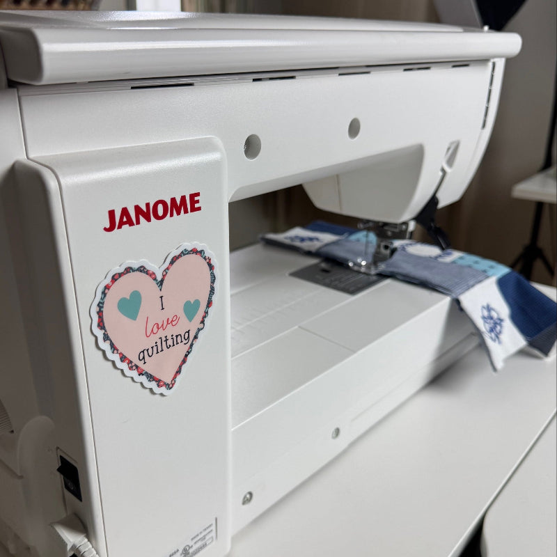 A Janome sewing machine with a I Love Quilting sticker.  A blue and white quilt project is on the machine