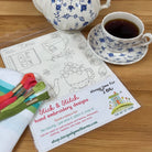 Tea set with teapot, cup, and saucer on a wooden table with a stick & stitch embroidery sheet