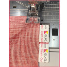 Sewing machine with a red fabric and a clear ruler attached, on a white background
