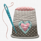 A quilted thimble with a pink floral top lining, a gray quilted body, a light blue heart applique, and a pink center heart, shown with a blue sewing needle on a white grid background.