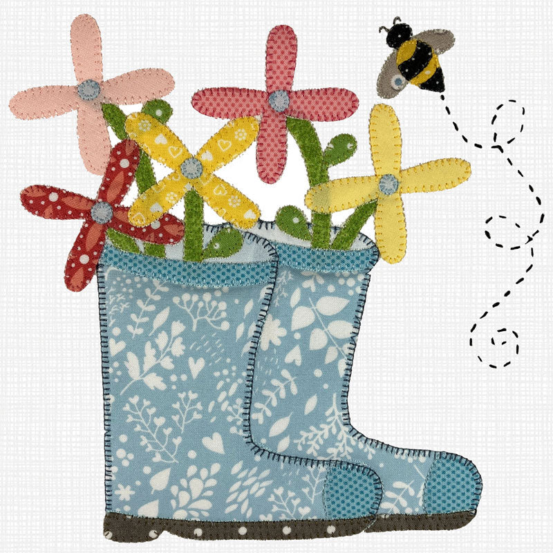 A whimsical applique design illustration of a pair of light blue rain boots filled with colorful flowers, including pink, red, yellow, and green blossoms, with a small bumblebee flying above on a white textured background.