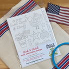 Patriotic design sheet on red and blue striped towel and American flag.
