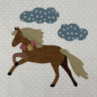 A quilted applique design of a brown horse with a beige mane and tail, decorated with pink and gold accents, set against a light beige floral fabric background with two blue patterned clouds.