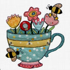A whimsical applique design of a teal teacup filled with colorful flowers and decorated with bumblebees, set against a white textured fabric background.